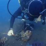 a scuba diver with good buoyancy cleans up some rusty metal and other marine pollution by taking part in a project aware environmental action called a Dive Against Debris